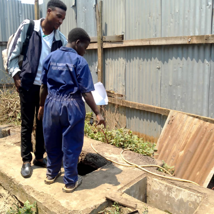 Christopher Tumusiime (left) a research assistant being shown by a sanitation worker some of the hazards when working around a septic tank.